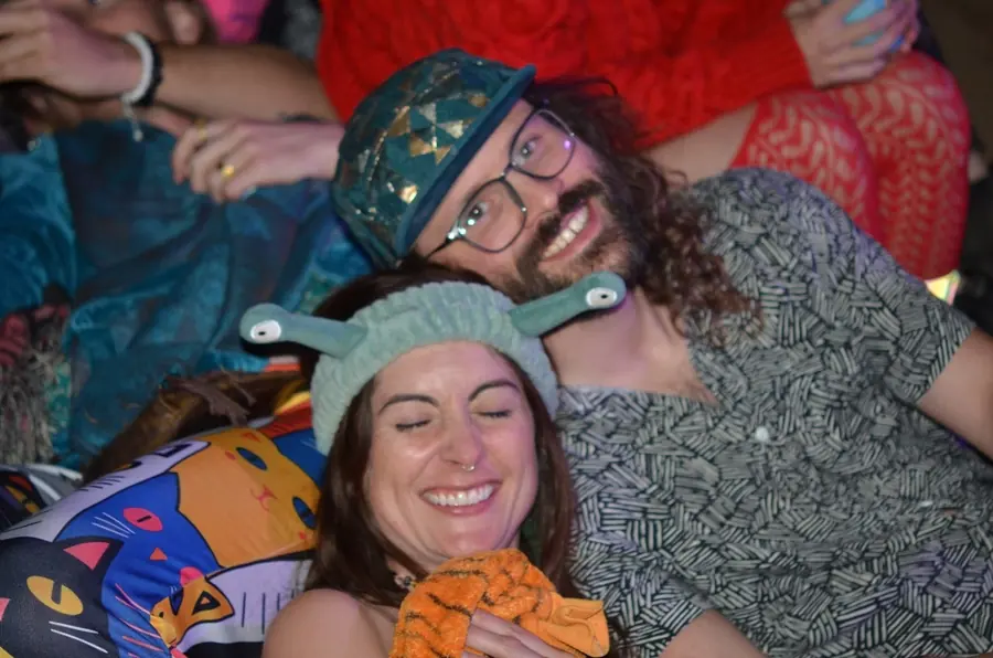Two friends lying back in a pile of cushions, grinning, one in a snail-antenna headband